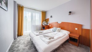 A hotel room with a bed, a bedside table, a chair, a desk with a fan, and a window with curtains. - Apartamenty Sun & Snow w Rezydencji Bielik (Miedzyzdroje)