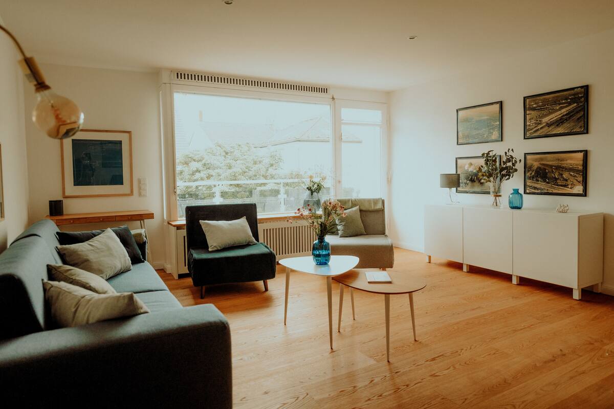 A modern living room with a sofa, a coffee table, and a view of the outdoors through large windows.