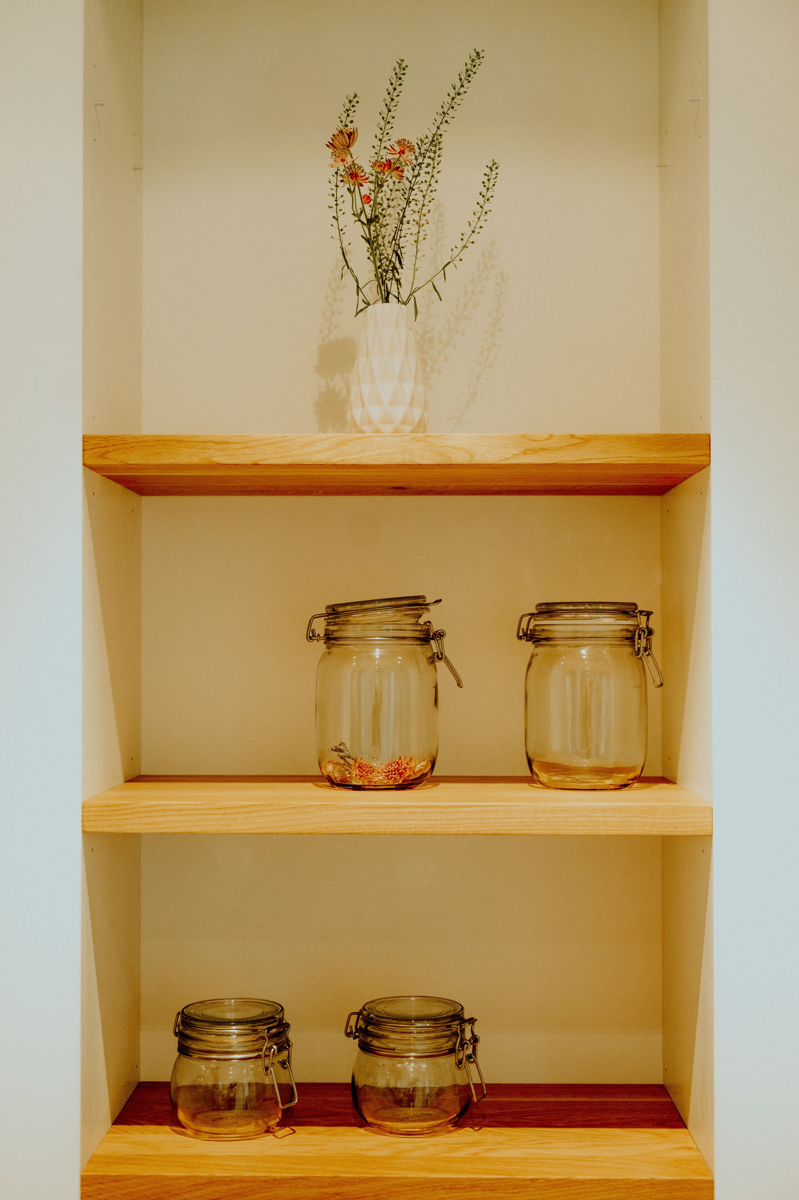 Three glass jars on wooden shelves, one with flowers.