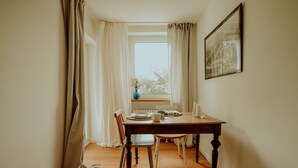 Un coin repas avec une table en bois, des chaises blanches, un vase de fleurs et une fenêtre avec des rideaux.