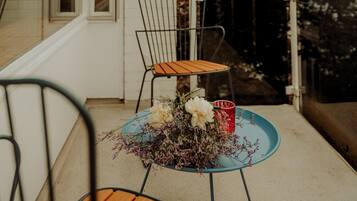 Una pequeña mesa exterior con sillas, un jarrón de flores y una taza roja en un balcón.