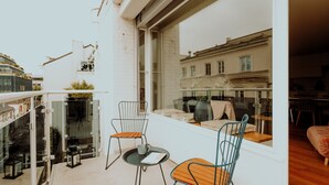 Un balcon avec deux chaises et une petite table, d’où l’on peut admirer un panorama sur la ville, avec ses bâtiments historiques.