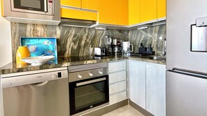 Een moderne keuken met gele kastjes, een Bosch vaatwasser, een magnetron, een koffiezetapparaat en een koelkast.