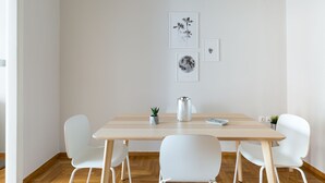 A minimalist dining area with a wooden table, white chairs, and wall art. - UPSTREET Urban Chic 1BD Apartment- Hilton area (Athens)