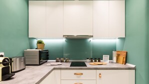 A modern kitchen with white cabinets, a built-in oven, a microwave, and a countertop with various appliances and utensils. - UPSTREET Urban Chic 1BD Apartment- Hilton area (Athens)