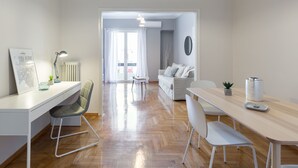 A modern living space with a white desk, a grey chair, a wooden dining table, and a white sofa. - UPSTREET Urban Chic 1BD Apartment- Hilton area (Athens)