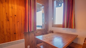 Une pièce aux murs lambrés, avec une table et des chaises en bois, une fenêtre avec des rideaux et un radiateur.