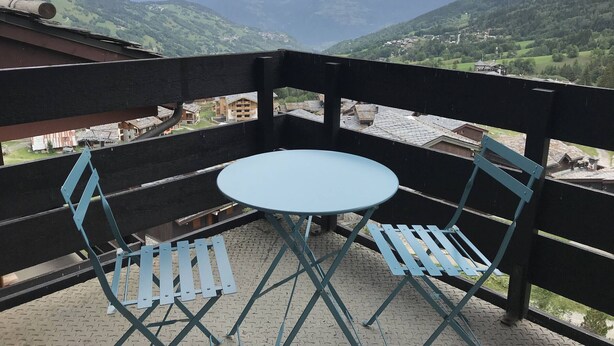 Un balcon avec une table et des chaises, donnant sur un paysage montagneux.