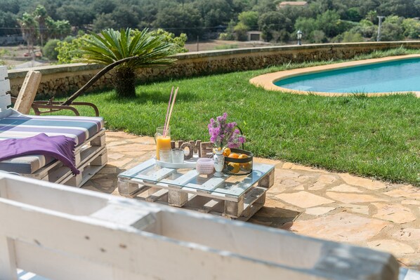 A poolside area with a glass table set with drinks, a flower vase, and a 'LOVE' sign.