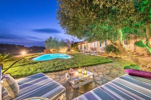 A poolside area with lounge chairs, a stone patio, and a well-lit outdoor space at dusk.