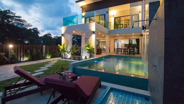 Una casa moderna de dos pisos con piscina, mobiliario exterior y un patio bien iluminado.