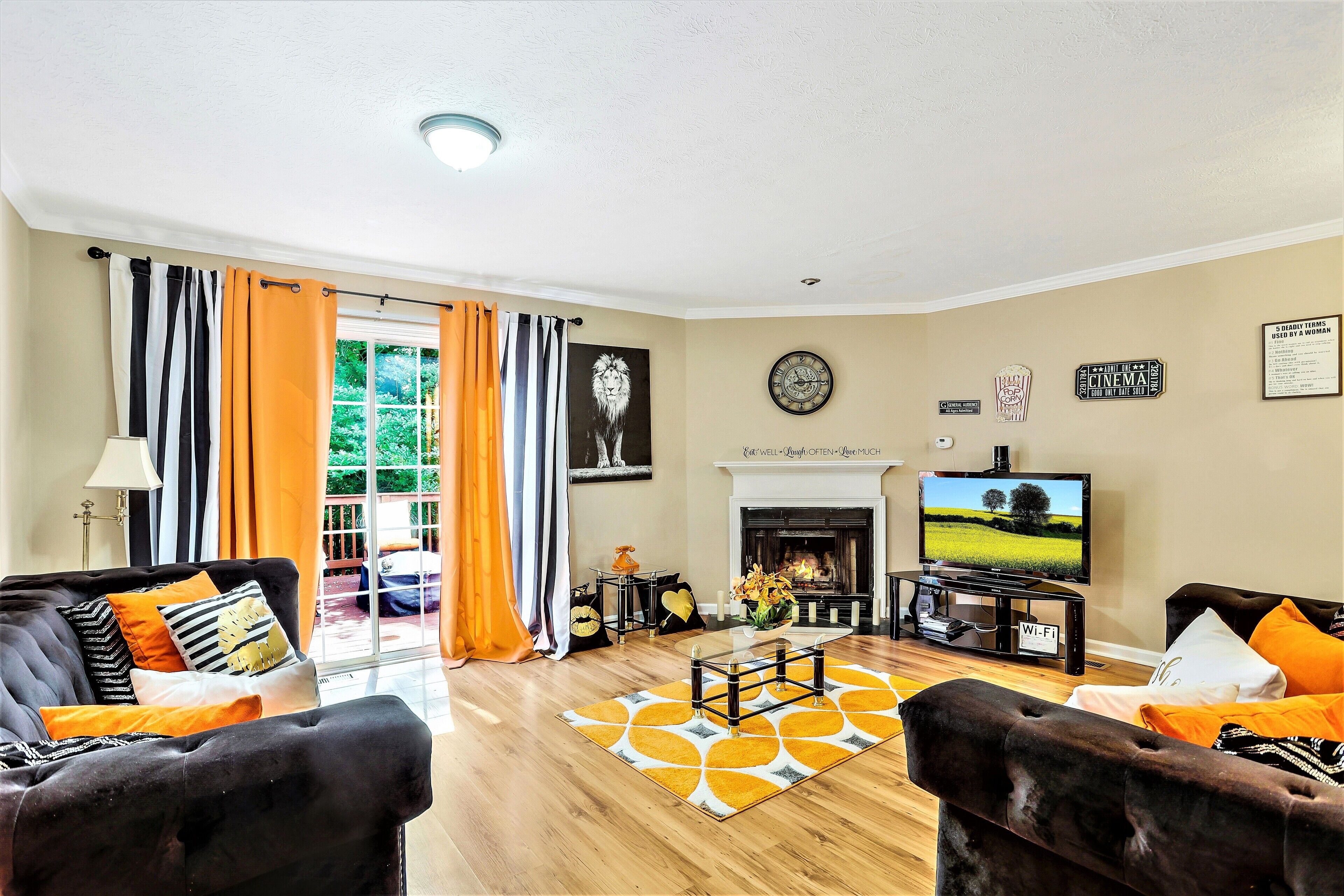 A living room with a fireplace, a television, and a view of the outdoors through a large window.