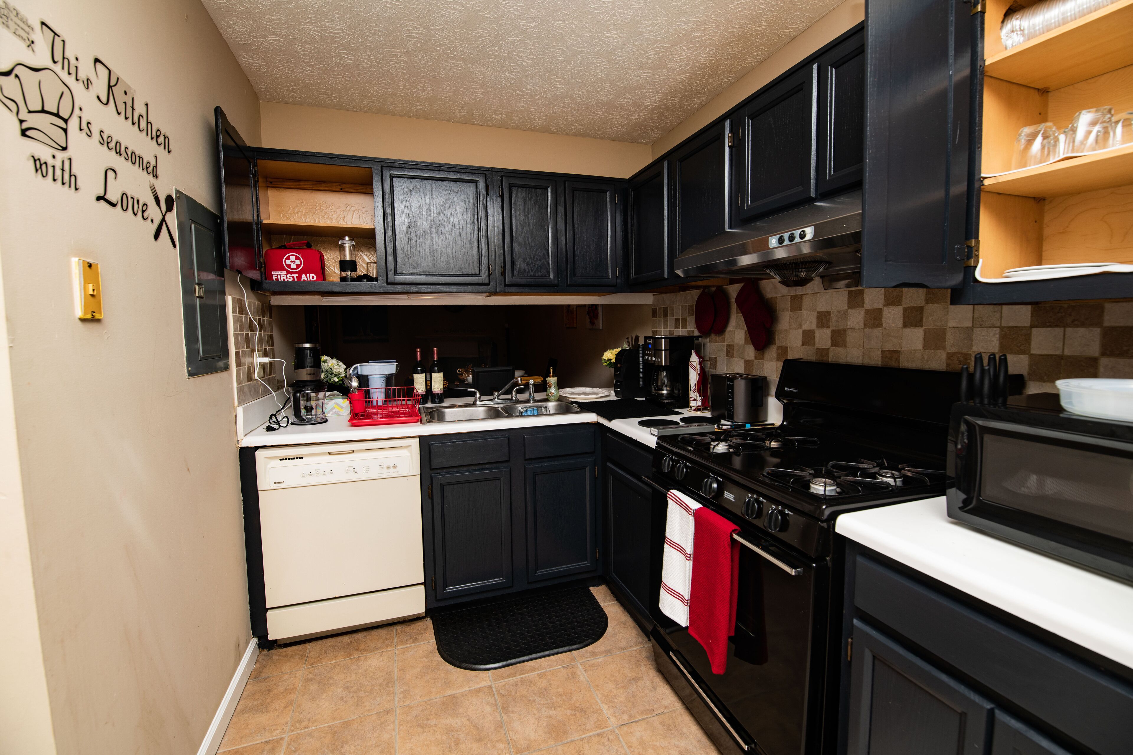 A compact kitchen with black cabinets, a stove, a dishwasher, and a coffee maker.