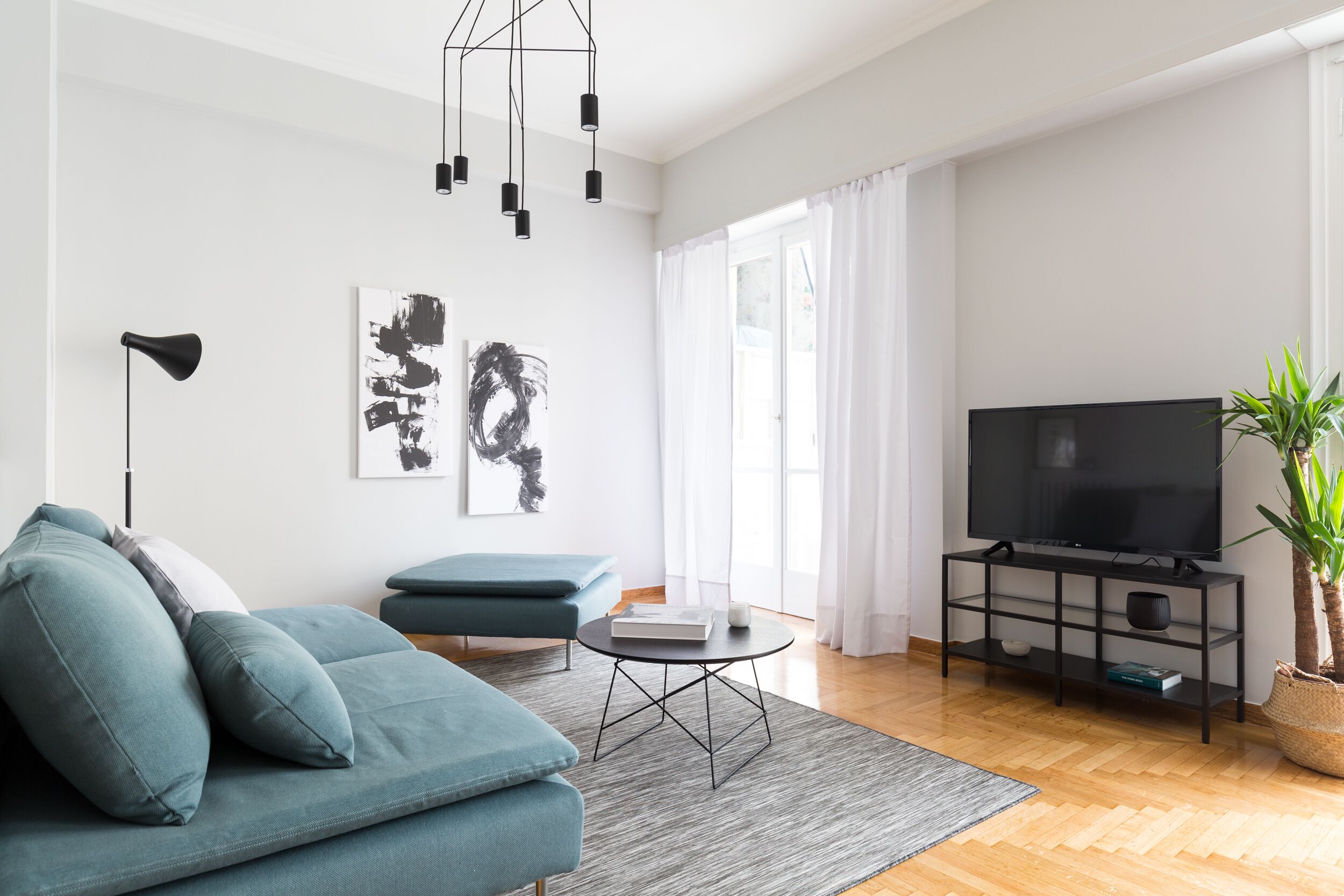 Ein modernes Wohnzimmer mit einem petrolfarbenen Sofa, einem schwarzen Fernseher auf einem Schrank und Kunstwerken an der Wand.