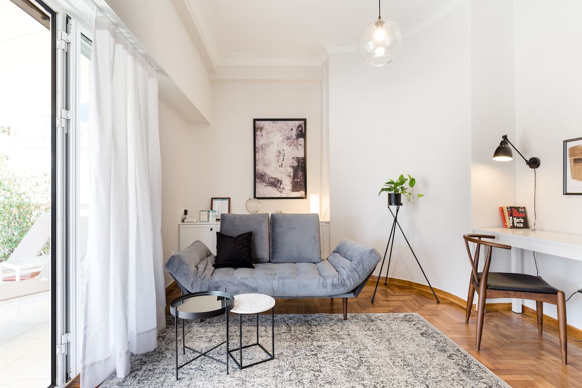 Una sala de estar moderna con un sofá gris, una mesita redonda pequeña, una lámpara de pie y una planta.