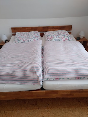 A double bed with floral and striped bedding, wooden headboard, bedside lamps, and a clock on the nightstand.