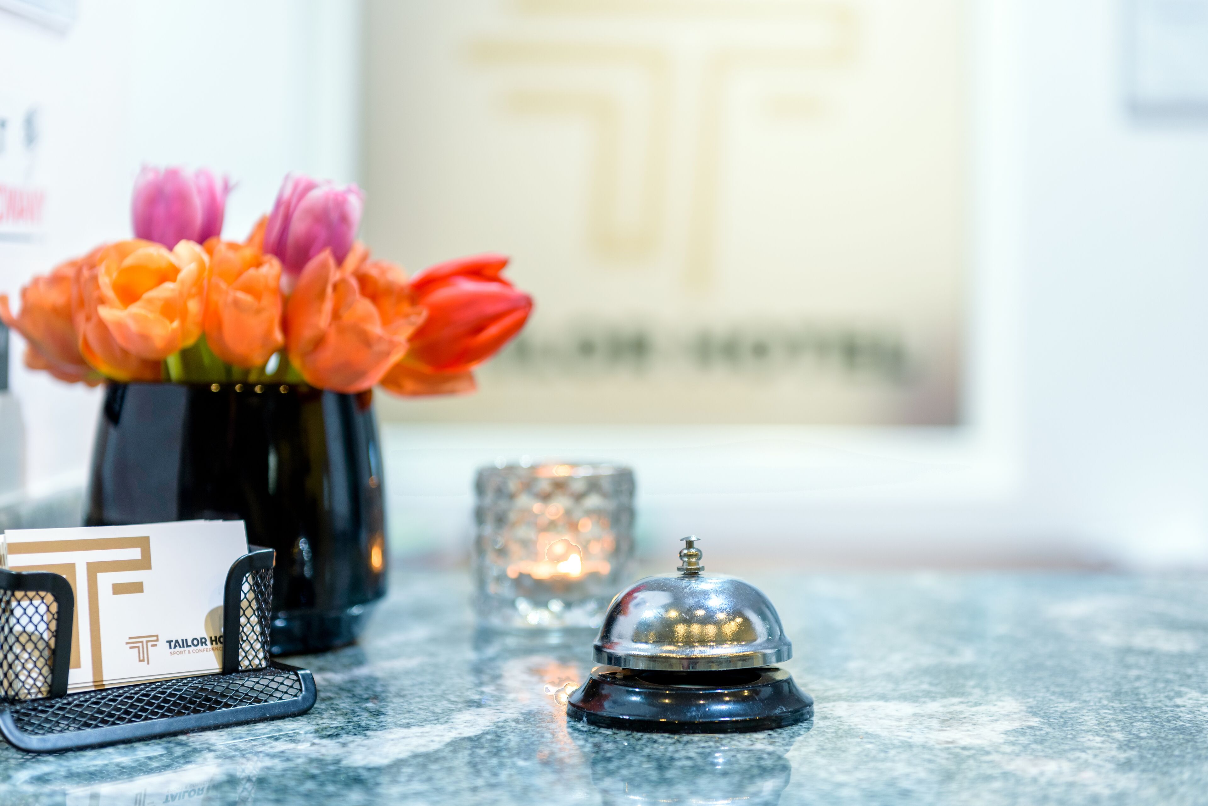 A hotel reception desk with a vase of flowers, a card holder, a glass candle, and a bell.