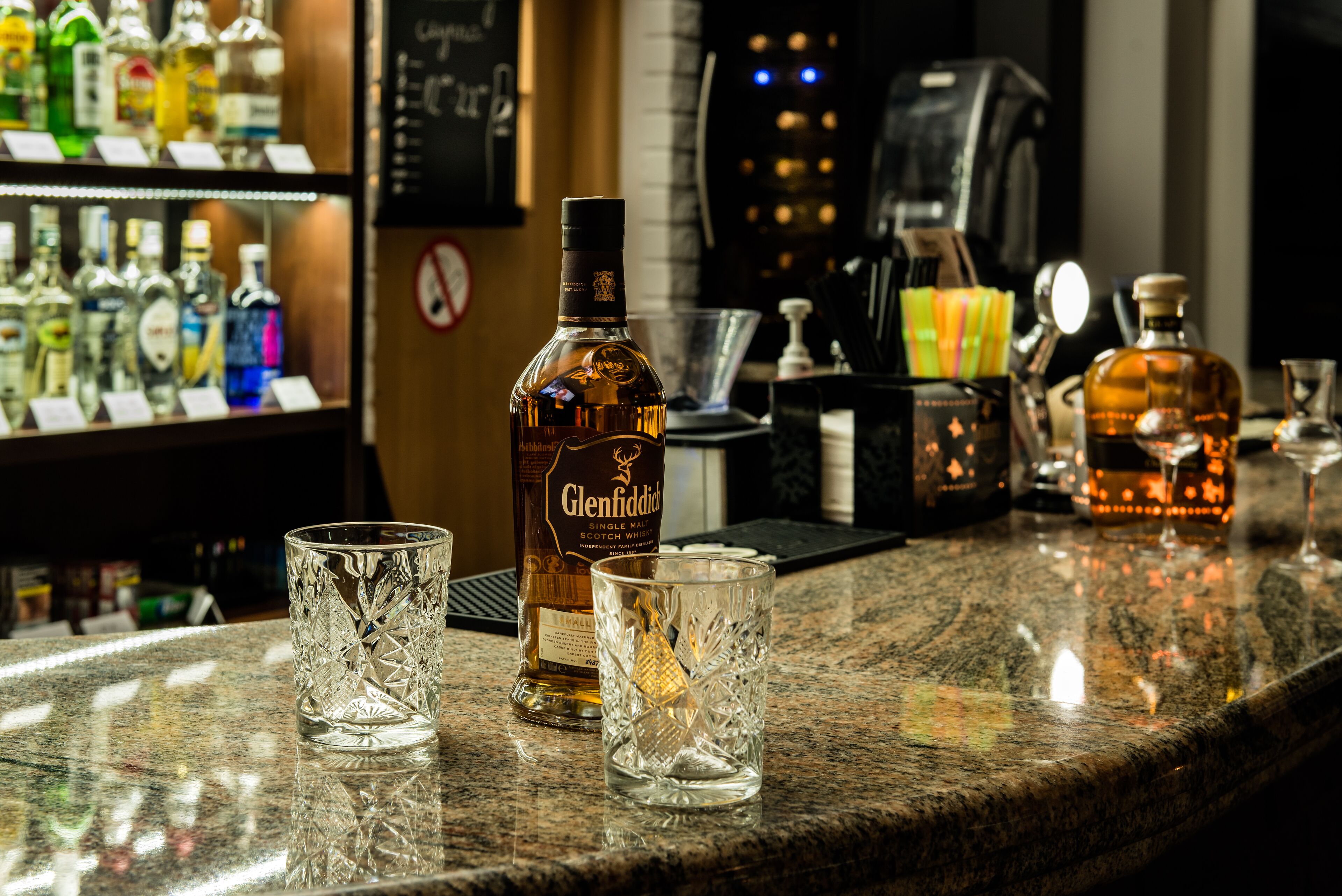 A bar counter with a bottle of Glenfiddich whisky, two glasses, and a coffee machine.
