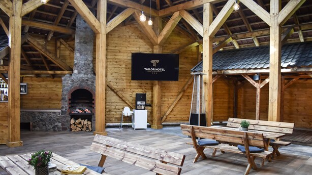 Un intérieur spacieux en bois, agrémenté d’une cheminée en pierre, de bancs en bois et d’une enseigne indiquant l’hôtel Tailor.