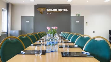 Una sala de conferencias en el Tailor Hotel con una larga mesa, sillas verdes, botellas de agua y un cartel que indica que es un espacio para deportes y conferencias.