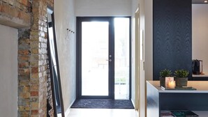 A modern kitchen with dark cabinetry and a small countertop. A door leads to a bright room with a view. - Søndergade - Strøget (Aarhus)