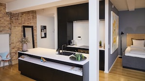 A modern kitchen with a large island, dark cabinetry, and a brick wall. - Søndergade - Strøget (Aarhus)