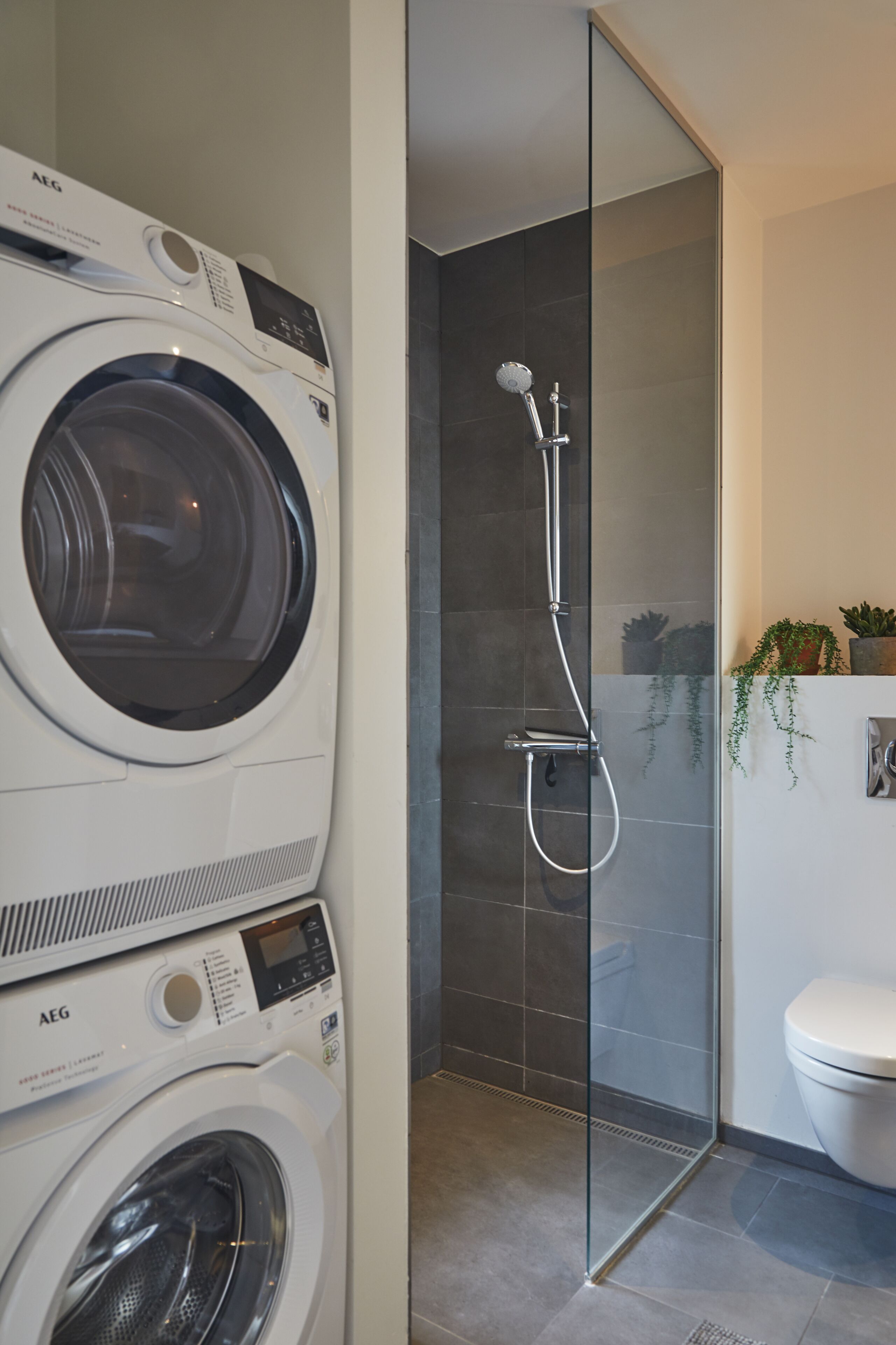 A modern bathroom with a washing machine, a glass-enclosed shower, and a toilet.