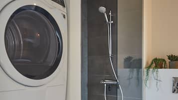A modern bathroom with a washing machine, a glass-enclosed shower, and a toilet.