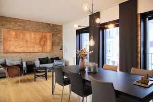Uma sala de jantar moderna com mesa de madeira escura, cadeiras estofadas cinzas e luminária pendente.