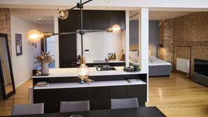 A modern kitchen with a central island, a dining area with a table and chairs, and a living area with a sofa and TV. - Søndergade - Strøget (Aarhus)