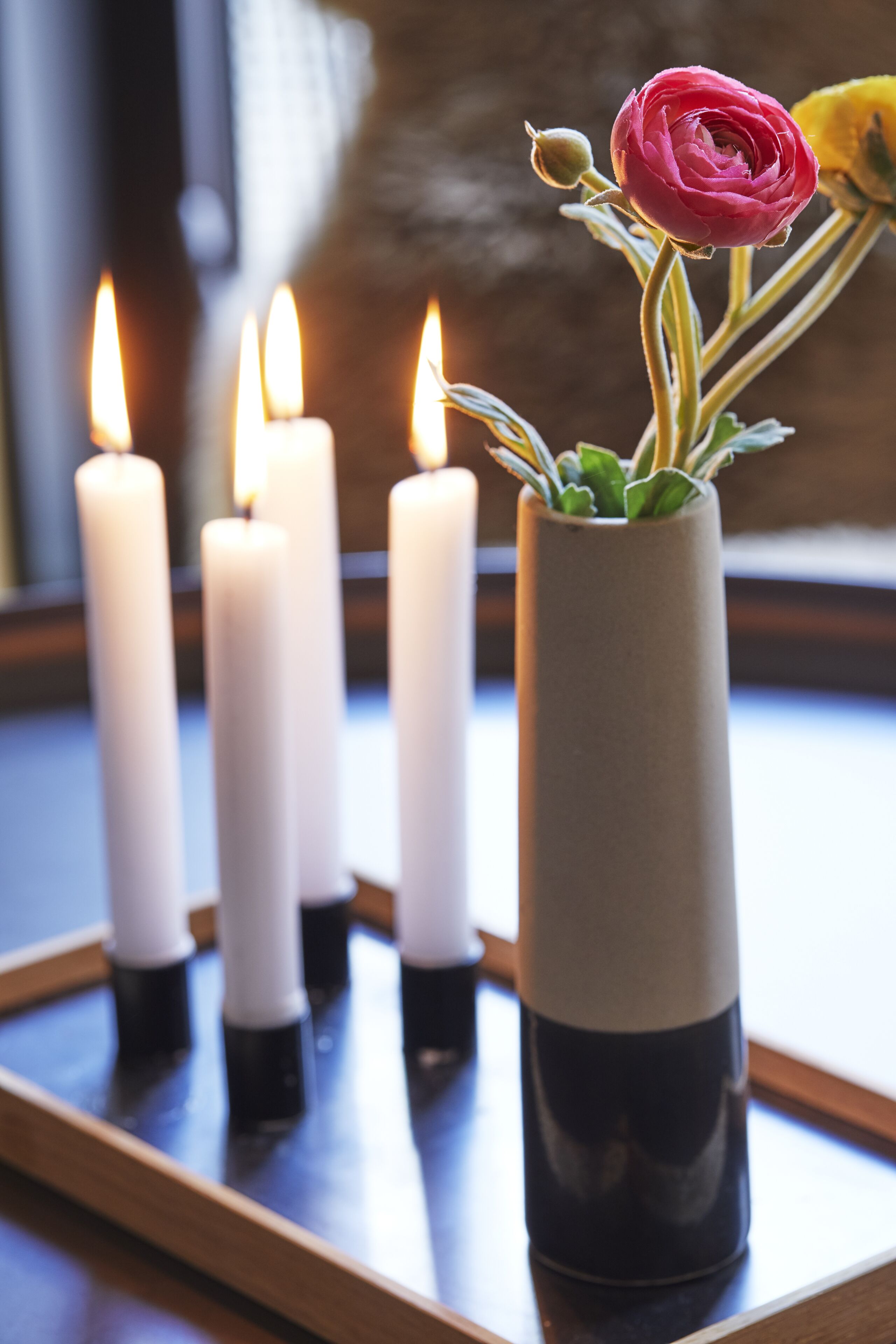 A tray with four lit candles and a vase with a flower.