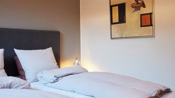 A hotel room with two beds, a headboard, a wall-mounted painting, and a bedside lamp.