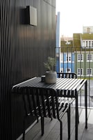 A balcony with a black metal table and chairs, a potted plant, and a view of colorful buildings.