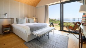 A bedroom with a large bed, a bench, a nightstand, and a view of the outdoors through a sliding door.