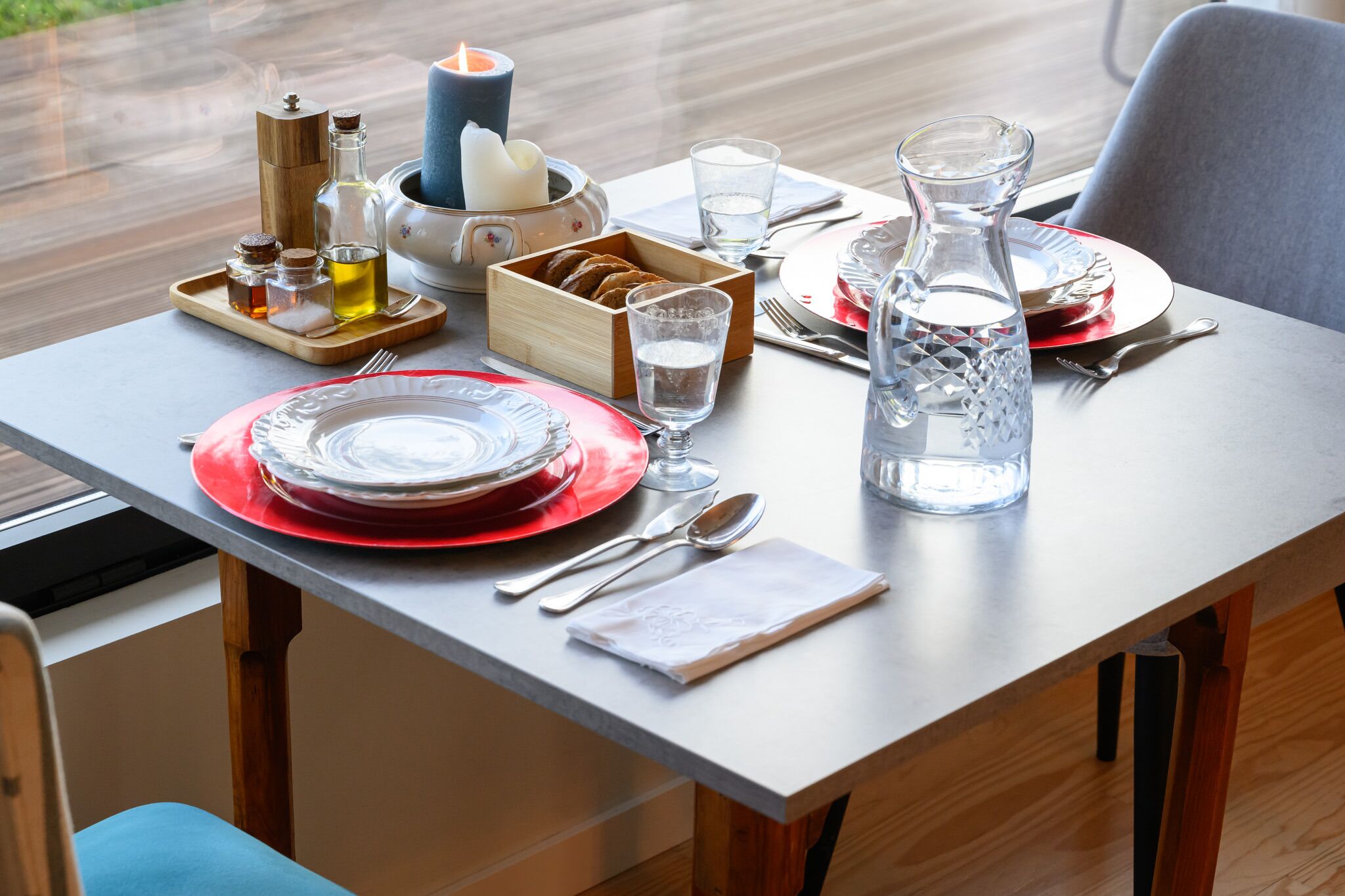 A dining table set with red plates, clear glasses, silverware, and a candle.