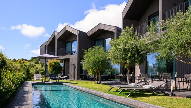 A modern building with a pool, outdoor seating, and greenery.
