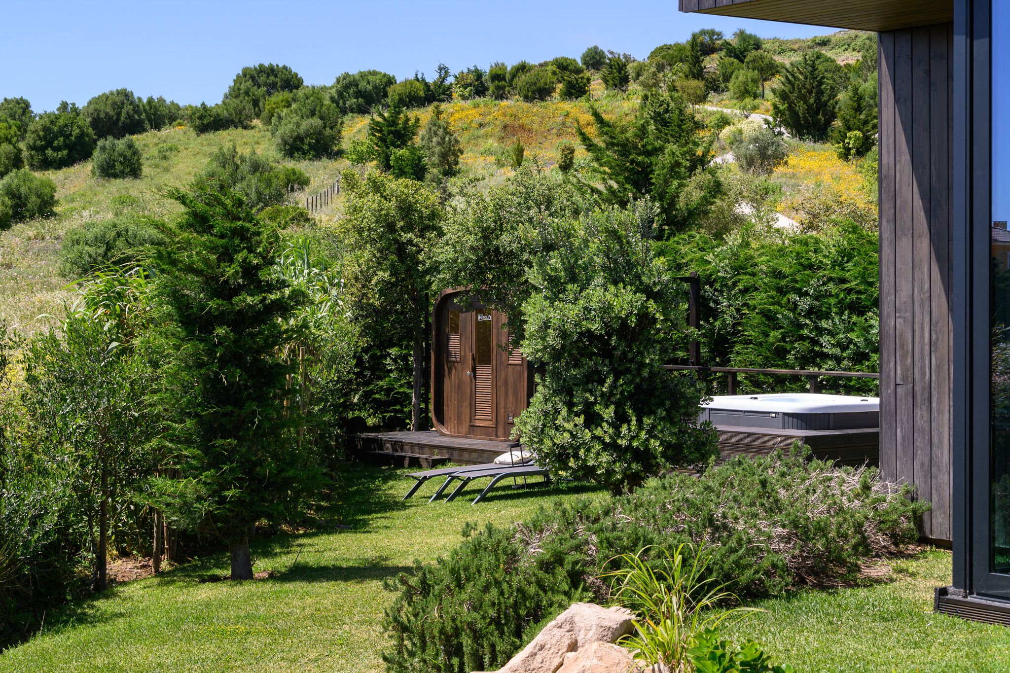 A wooden cabin with a deck, surrounded by lush greenery and trees.