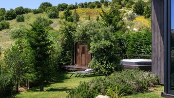 A wooden cabin with a deck, surrounded by lush greenery and trees.