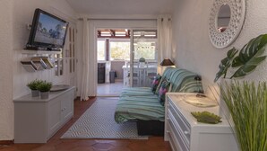 Una camera compatta con un letto, comodino, televisore e vista del balcone.