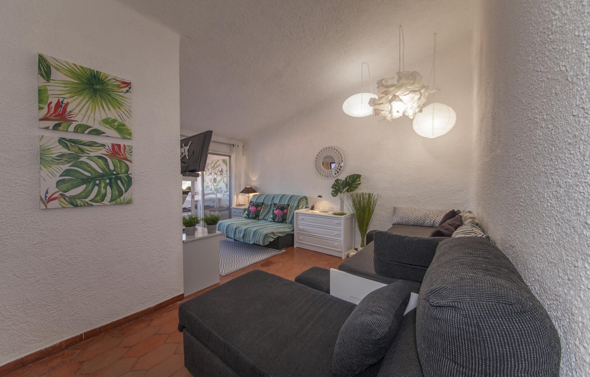 Ein gemütlicher Wohnraum mit einer Sofagarnitur, einem Fernseher und einer Deckenleuchte.