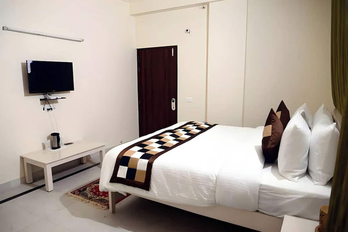 A hotel room with a bed, a TV mounted on the wall, a bedside table, a desk, and a door.