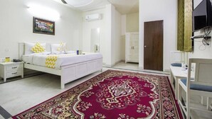 A bedroom with a bed, nightstands, a desk, a television, and a ceiling fan. - Hotel Dior Near Jal Mahal, Jaipur (Jaipur)