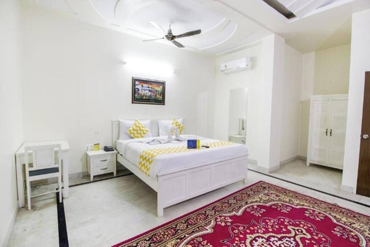 A bedroom with a bed, a nightstand, a desk, a ceiling fan, a wardrobe, and a red patterned rug.