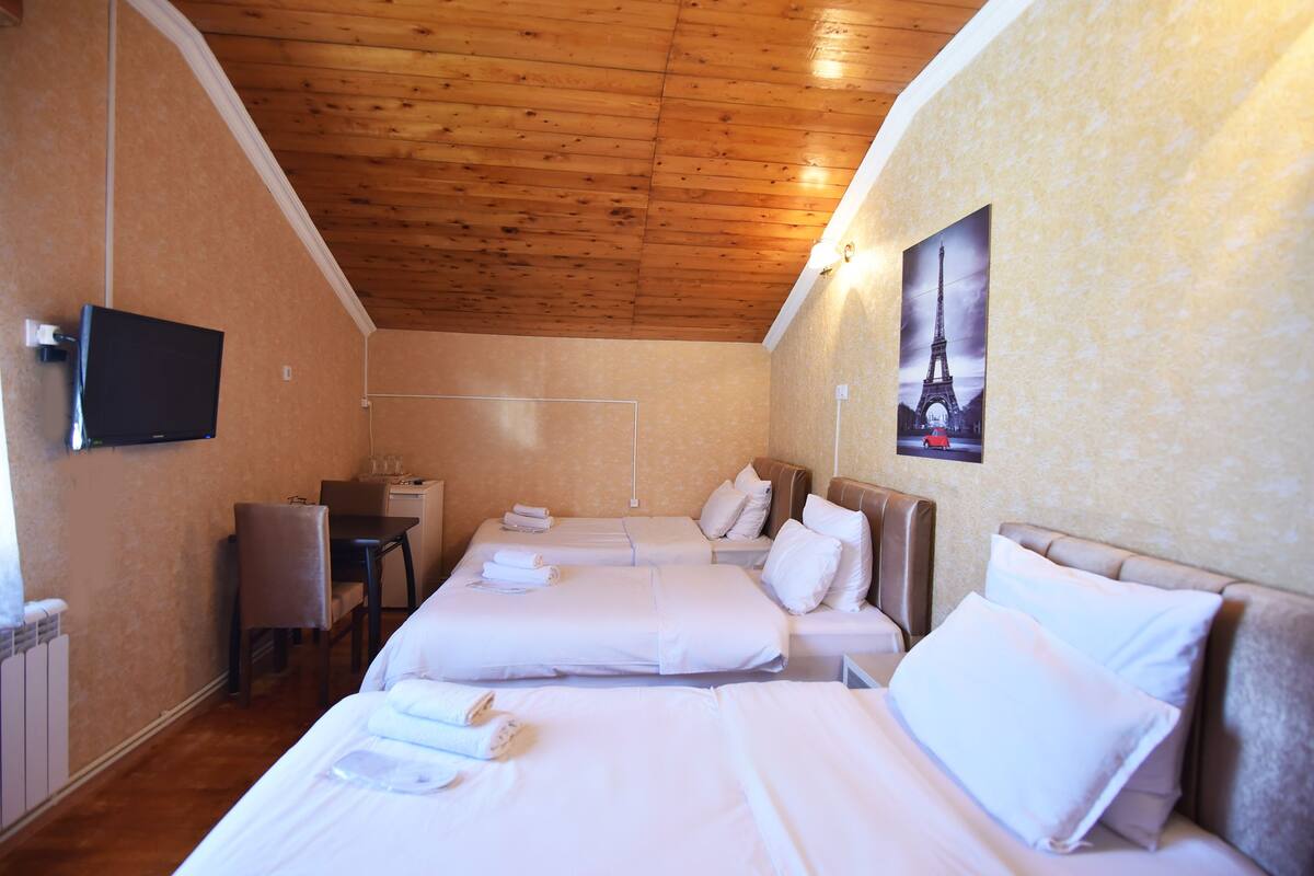 A hotel room with two beds, a desk, a chair, and a television on the wall.