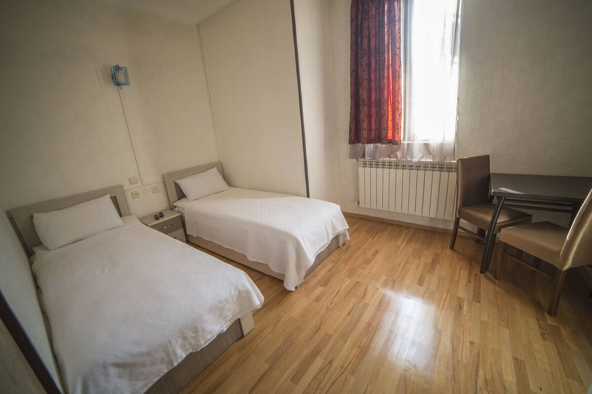 A room with two single beds, a desk, and a chair.