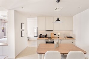 A modern kitchen with white cabinets, a wooden dining table, and a pendant light. - UPSTREET Luxury Apartments in Plaka (Athens)