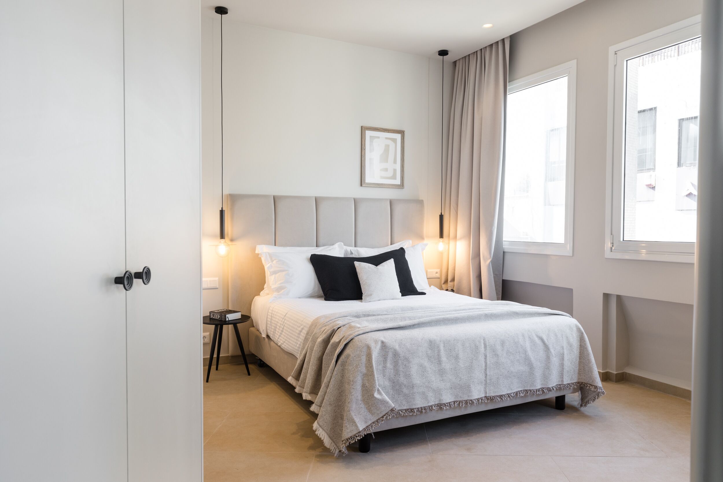 Un dormitorio moderno con cama, mesitas de noche, un cuadro enmarcado en la pared y una ventana con cortinas.