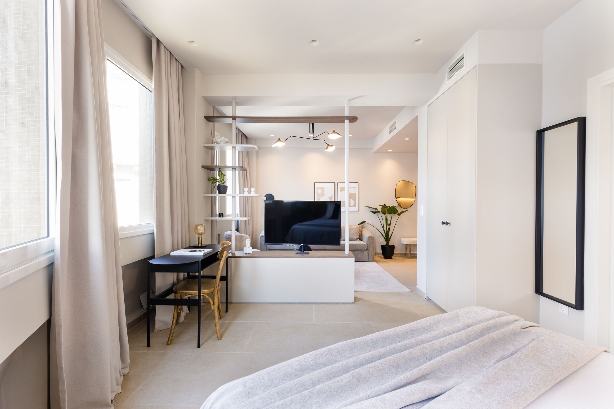 Un dormitorio moderno con una cama, un escritorio y una silla. Hay un televisor y una planta en la habitación.