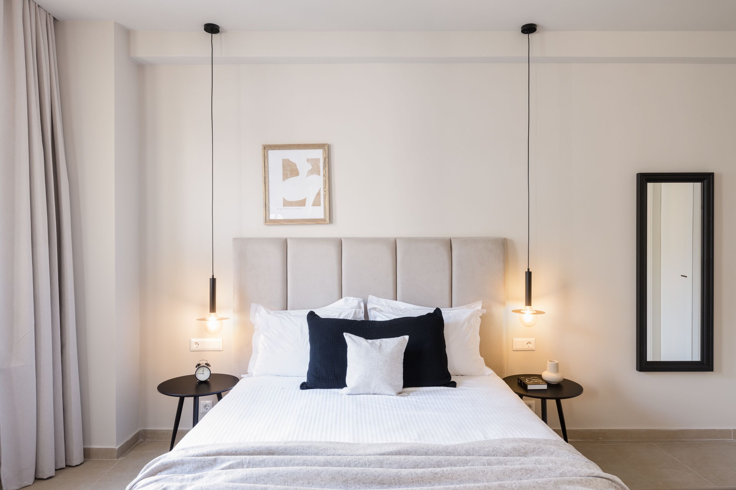 Habitación de hotel ordenada con una cama grande, dos mesitas de noche, una lámpara de noche, una obra de arte enmarcada y un espejo en la pared.