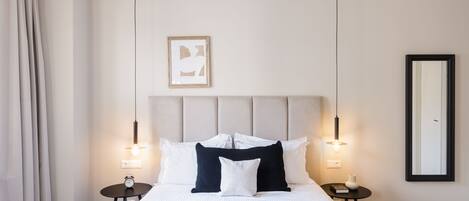 Habitación de hotel ordenada con una cama grande, dos mesitas de noche, una lámpara de noche, una obra de arte enmarcada y un espejo en la pared.